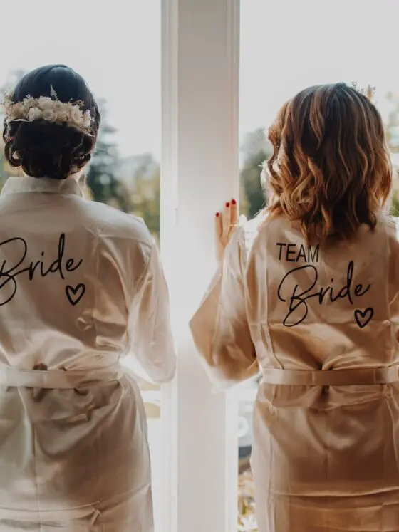 two bridesmaids in robes looking out a window - Trauzeuge Aufgaben