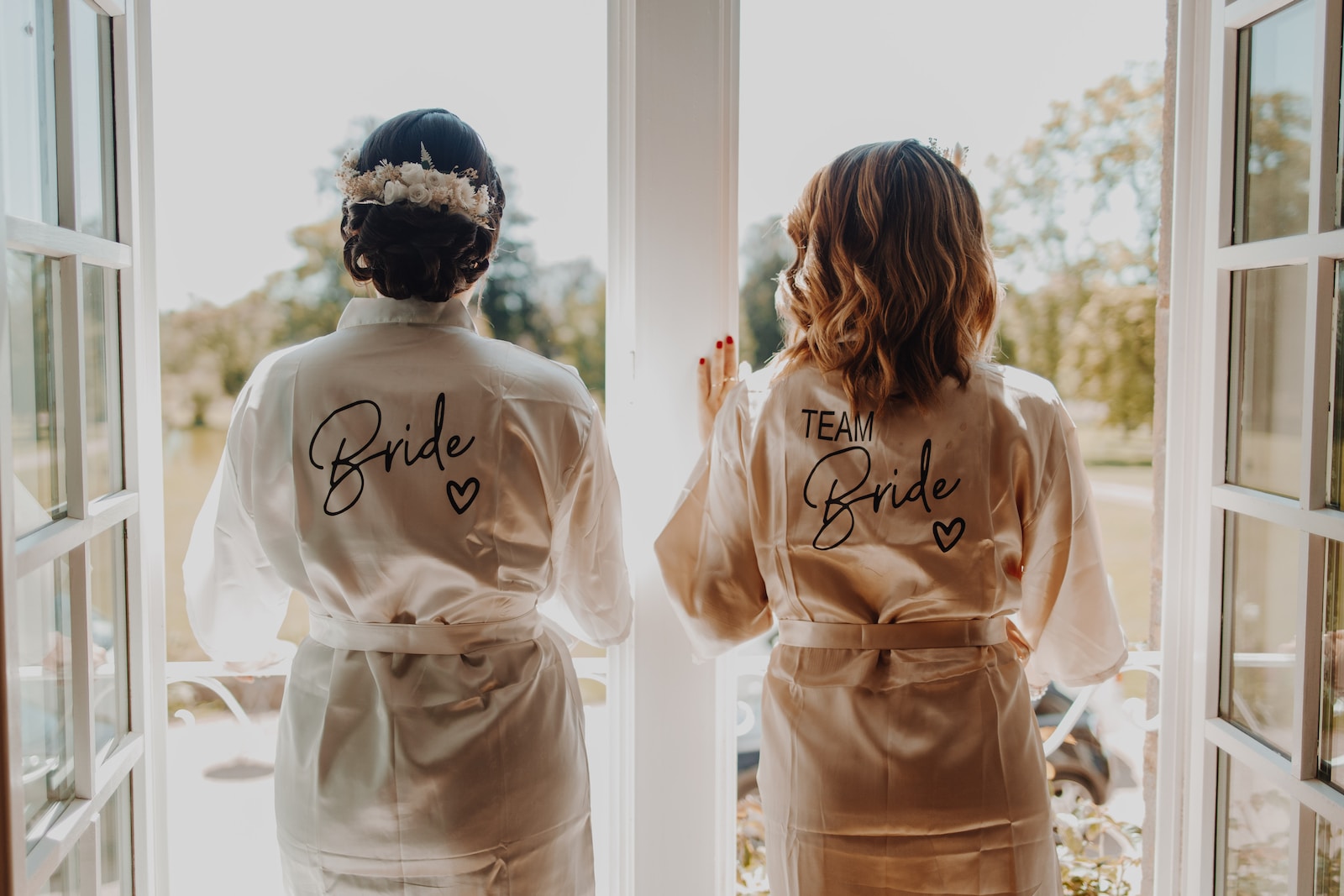 two bridesmaids in robes looking out a window - Trauzeuge Aufgaben